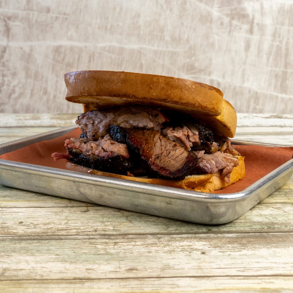 Gatlin's BBQ brisket sandwich on toasted bread, served on a metal tray with brown paper.