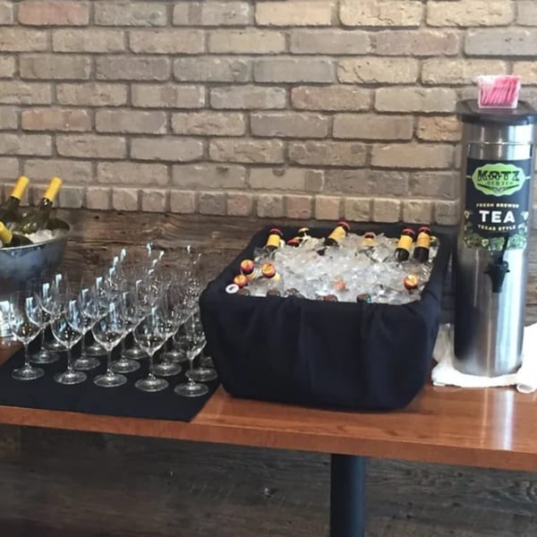 Beverage station with wine bottles in ice, beer in a cooler, wine glasses, and a tea dispenser.