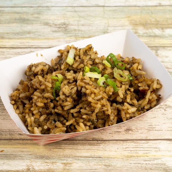 Gatlin's BBQ dirty rice with green onions in a white paper tray on a wooden table.