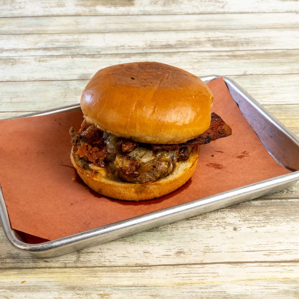 Gatlin's BBQ burger with bacon, melted cheese, and caramelized onions on a metal tray.