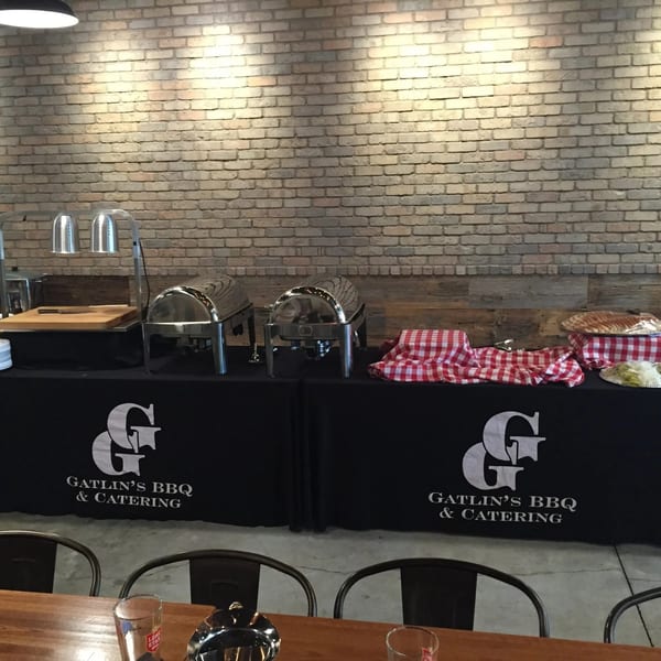 Gatlin's BBQ catering setup with chafing dishes, cutting board, and red checkered tablecloths.