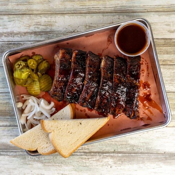 Gatlin's BBQ ribs with sauce, pickles, onions, and white bread on a metal tray.