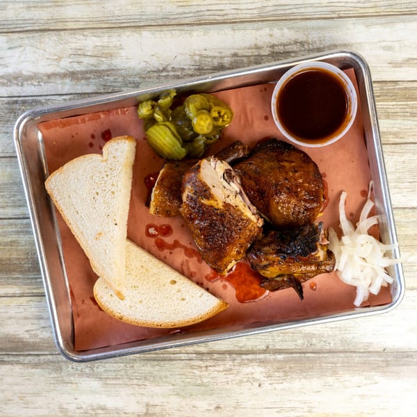 Gatlin's BBQ chicken plate with sliced bread, pickles, onions, and barbecue sauce on a metal tray.