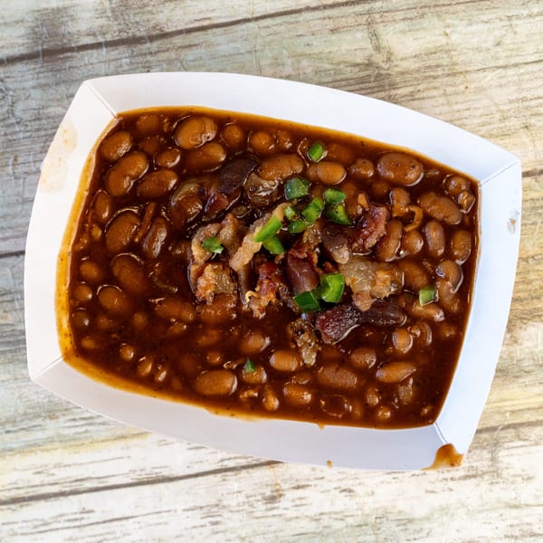 Gatlin's BBQ baked beans with chopped meat and green onions in a white paper tray.
